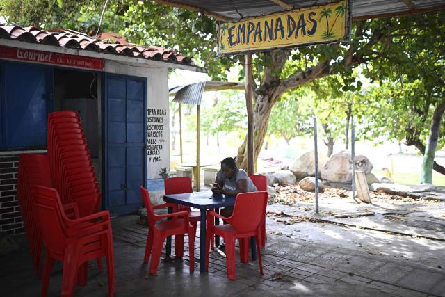 Faisuris Alvarez, 39, uses a mobile phone outside her empanadas stand in Naiguata, La Guaira state, Venezuela on July 8, 2026, following the June 24 earthquakes. Venezuela's government called on July 8, 2026 for the release of frozen assets to help raise funds for the country's recovery from last month's twin earthquakes that killed at least 3,600 people. (Photo by Federico PARRA / AFP)