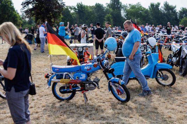 A man looks at a Simson moped featuring an advert for the far-right Alternative for Germany (AfD) party's during an election campaign event of the far-right Alternative for Germany (AfD) party's and a motorbike and moped ride in Jessnitz, eastern Germany on June 28, 2026. Fans of far-right Alternative for Germany party's top candidate for the regional elections in Saxony-Anhalt, Ulrich Siegmund joined him for a countryside ride on Simson-brand scooters, that have become a symbol of East German identity. Descendants of the Simson firm's namesake Jewish founders, who gave up the company to escape persecution in Nazi Germany, have denounced the AfD's appropriation of the brand name. (Photo by Jens SCHLÜTER / AFP)