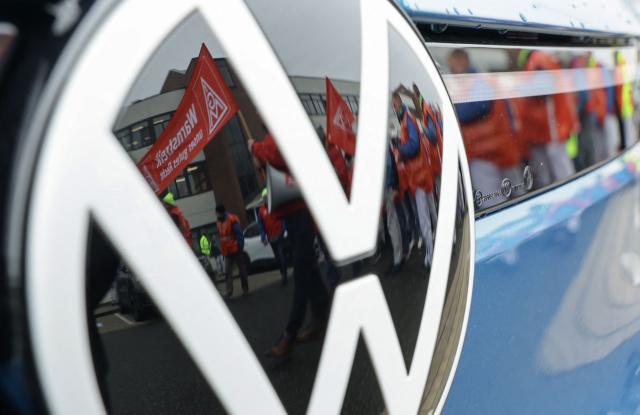A picture taken on December 2, 2024 shows employees of Volkswagen (VW) reflected in the logo of a VW car as they demonstrate in front of the plant of German car maker Volkswagen (VW), in Zwickau, eastern Germany. German auto giant Volkswagen's management meet on July 9, 2026 to thrash out plans for what could be the biggest ever restructuring in the global auto industry with unions set to protest any mass job cuts. (Photo by Jens Schlueter / AFP) / ALTERNATIVE CROP