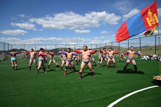 This photo taken on June 24, 2026 shows Mongolian wrestlers performing a bird dance at a training camp ahead of the Naadam Festival on the outskirts of Ulaanbaatar. The whistle blows, sending dozens of hulking wrestlers chasing a football in the Mongolian grasslands -- a World Cup twist in their gruelling training for one of the country's oldest sporting traditions. (Photo by Adek BERRY / AFP) / To go with 'MONGOLIA-LIFESTYLE-TRADITION-WRESTLING,FOCUS' by Mungunsor Purevsuren