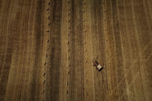 This aerial photograph shows a tractor and baler standing in a harvested field dotted with round straw bales after an early cereal harvest brought forward by a summer heatwave near Ségalas, some 35 kilometres from Marmande, south-western France, on July 8, 2026. (Photo by Philippe LOPEZ / AFP)