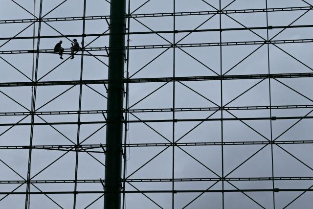 Workers sit on the metal framework of a billboard during maintenance work in Bengaluru on July 9, 2026. (Photo by Idrees MOHAMMED / AFP)