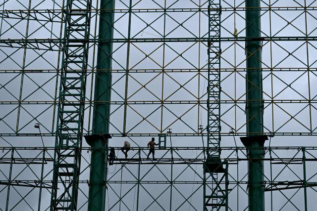 Workers stand on the metal framework of a billboard during maintenance work in Bengaluru on July 9, 2026. (Photo by Idrees MOHAMMED / AFP)
