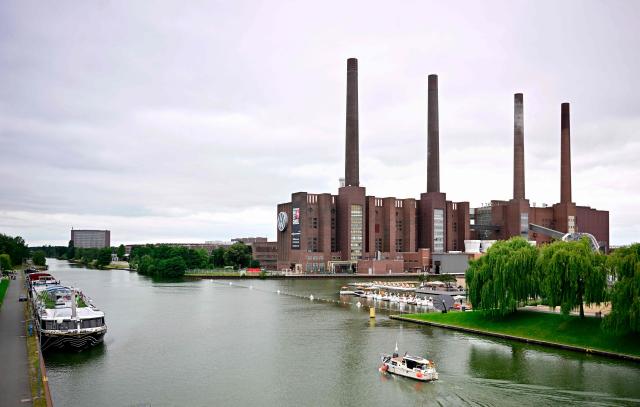 A general view taken on July 9, 2026 shows a boat passing on the Mittelland Canal in front of the Wolfsburg Volkswagen (VW) Plant in Wolfsburg, Germany, prior to a planned rally of VW employees called by German trade union IG Metall to protest against restructuring and mass job cut plans at the VW headquarters in Wolfsburg, Germany. IG Metall is organising protests by VW workers outside plants across the country on July 9, when the carmaker's bosses will present the restructuring plans to the supervisory board. Europe's largest carmaker has come under intense pressure from US tariffs, slimmer profit margins from electric cars and above all intense competition in China, the world's largest auto market. VW, whose 10 brands range from mass-market Seats to premium Porsches, is already in the process of axing 50,000 jobs in Germany by 2030, including 35,000 at its namesake marque. (Photo by Tobias SCHWARZ / AFP)