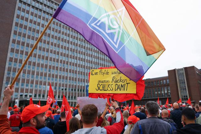 Volkswagen (VW) employees, one with a rainbow coloured IG Metall flag, attend a rally to protest against restructuring and mass job cut plans at the VW headquarters on July 9, 2026 at the Wolfsburg Volkswagen Plant in Wolfsburg, northern Germany. IG Metall is organising protests by VW workers outside plants across the country on July 9, when the carmaker's bosses will present the restructuring plans to the supervisory board. Europe's largest carmaker has come under intense pressure from US tariffs, slimmer profit margins from electric cars and above all intense competition in China, the world's largest auto market. VW, whose 10 brands range from mass-market Seats to premium Porsches, is already in the process of axing 50,000 jobs in Germany by 2030, including 35,000 at its namesake marque. (Photo by Lisi Niesner / POOL / AFP)