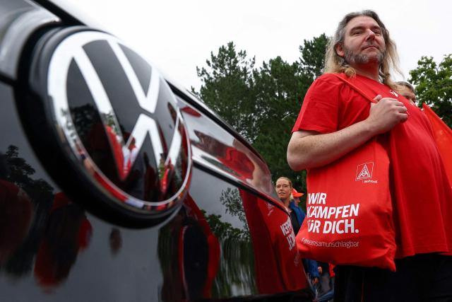 Volkswagen (VW) employees, one with an IG Metall bag, attend a rally to protest against restructuring and mass job cut plans at the VW headquarters on July 9, 2026 at the Wolfsburg Volkswagen Plant in Wolfsburg, northern Germany. IG Metall is organising protests by VW workers outside plants across the country on July 9, when the carmaker's bosses will present the restructuring plans to the supervisory board. Europe's largest carmaker has come under intense pressure from US tariffs, slimmer profit margins from electric cars and above all intense competition in China, the world's largest auto market. VW, whose 10 brands range from mass-market Seats to premium Porsches, is already in the process of axing 50,000 jobs in Germany by 2030, including 35,000 at its namesake marque. (Photo by Lisi Niesner / POOL / AFP)