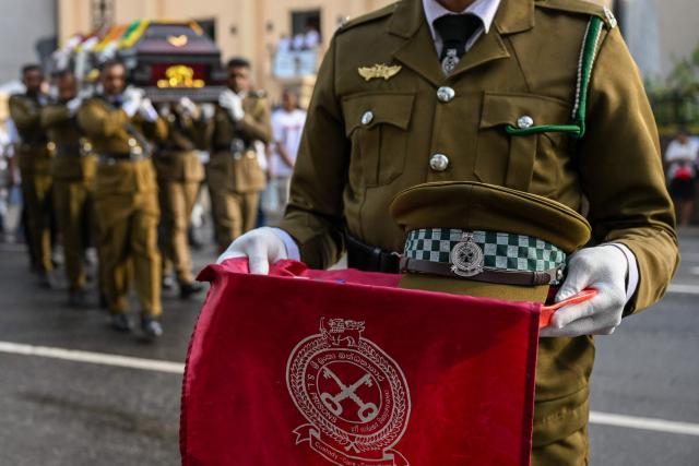 An officer carries the service cap and medals of prison jailer S.H.G. Chandrawansha, killed in Negombo prison riot, during his funeral ceremony in Colombo on July 9, 2026. Sri Lanka launched an investigation on July 7 into its deadliest prison riot in years, as the death toll from clashes between rival drug gangs rose to 27. (Photo by Ishara S. KODIKARA / AFP)