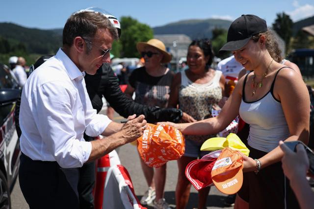 France's President Emmanuel Macron signs promotional hats handed to spectators by sponsors on the sidelines of the 6th stage of the 113th edition of the Tour de France cycling race, 186,2 km between Pau and Gavarnie-Gèdre in the French Pyrenees, on July 9, 2026. (Photo by Anne-Christine POUJOULAT / AFP)
