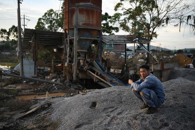 A man rests beside a factory that makes gravel for roads, which was damaged by flood waters, in Gantang in China’s southwest Guangxi region on July 9, 2026. The death toll from devastating floods in southern China's Guangxi region rose to 39 on July 9, with nine people still missing, state media reported, as residents went about cleaning up. (Photo by GREG BAKER / AFP)