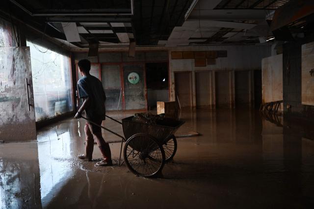 A man hauls equipment from a store that was flooded when a reservoir collapsed in Gantang, in China’s southwest Guangxi region, on July 9, 2026. The death toll from devastating floods in southern China's Guangxi region rose to 39 on July 9, with nine people still missing, state media reported, as residents went about cleaning up. (Photo by GREG BAKER / AFP)