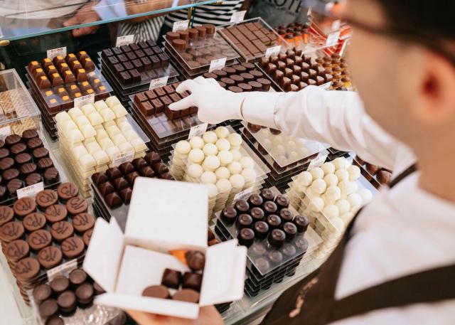 A vendor picks chocolates from a booth for a client at a Neuhaus chocolatier shop of the Koninginnegalerij - Galerie de la Reine, in the city center of Brussels on July 9, 2026. (Photo by Marius BURGELMANS / Belga / AFP) / Belgium OUT