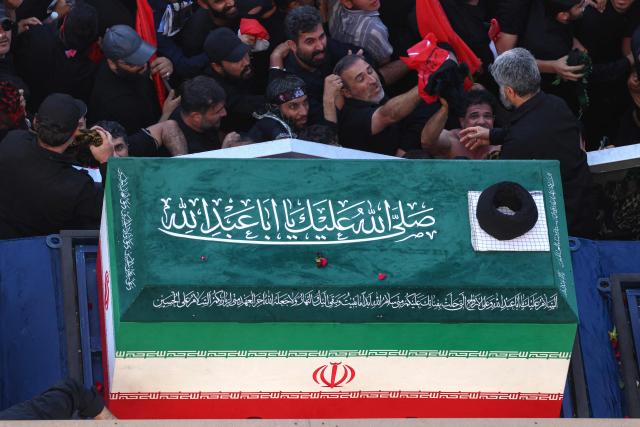 Crowds of mourners surround the convoy carrying the coffins of Iran's slain supreme leader Ali Khamenei and members of his family during a funeral procession, before he is buried at the Shrine of Imam Reza, Iran's most revered place of worship, in Mashhad on July 9, 2026. Braving sweltering heat and calling for revenge, Iranians loyal to the Islamic republic massed on July 9 for the burial of slain supreme leader Ali Khamenei in his hometown of Mashhad. (Photo by ATTA KENARE / AFP) / 