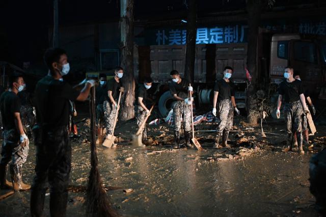Security personnel clean mud from a road that was flooded when a reservoir collapsed in Gantang, in China’s southwest Guangxi region on July 9, 2026. The death toll from devastating floods in southern China's Guangxi region rose to 39 on July 9, with nine people still missing, state media reported, as residents went about cleaning up. (Photo by GREG BAKER / AFP)
