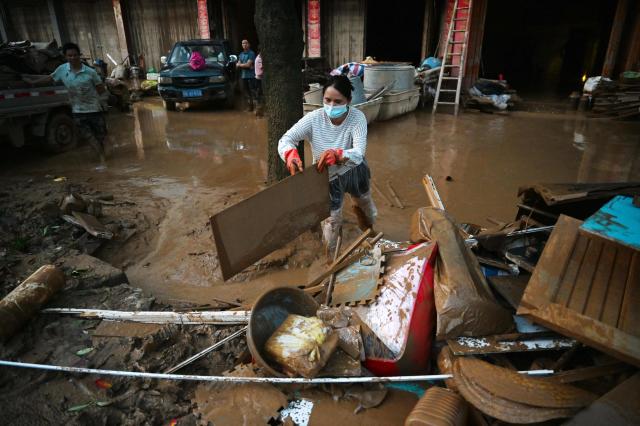A woman clears equipment from a house during a cleanup operation in Gantang after it was flooded when a nearby reservoir collapsed in China’s southwest Guangxi region on July 9, 2026. The death toll from devastating floods in southern China's Guangxi region rose to 39 on July 9, with nine people still missing, state media reported, as residents went about cleaning up. (Photo by GREG BAKER / AFP)