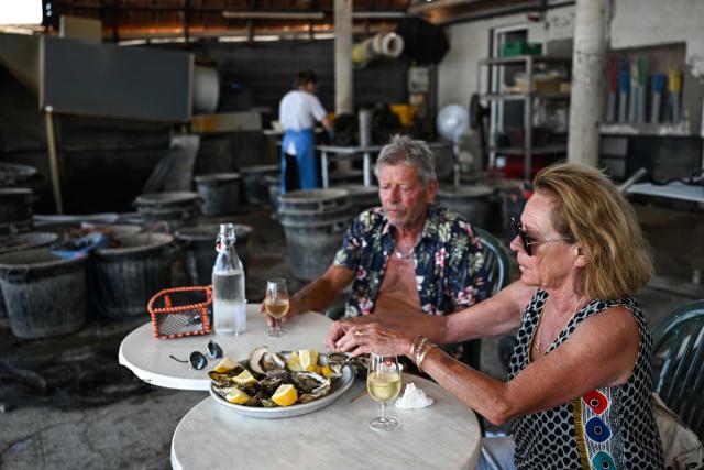 A couple of tourists eat oysters at Huitres de Bouzigues' farm, on the Etang de Thau in Loupian, southern France, on July 9, 2026. (Photo by Gabriel BOUYS / AFP)