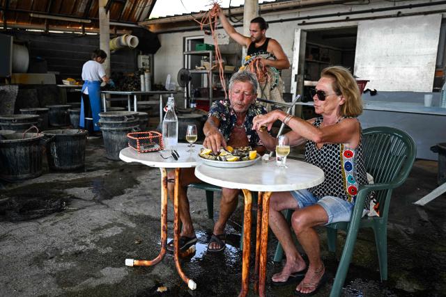 A couple of tourists eat Oysters at Huitres de Bouzigues' farm, on the Etang de Thau in Loupian, southern France, on July 9, 2026. (Photo by Gabriel BOUYS / AFP)