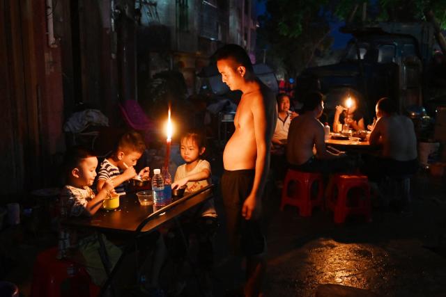 A father looks on as children have dinner by candlelight outside a house in Gantang after electricity was knocked out by floodwaters from a collapsed reservoir in China’s southwest Guangxi region on July 9, 2026. The death toll from devastating floods in southern China's Guangxi region rose to 39 on July 9, with nine people still missing, state media reported, as residents went about cleaning up. (Photo by GREG BAKER / AFP)