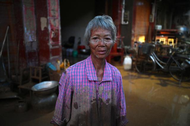 A woman stands outside her house in Gantang after it was flooded when a nearby reservoir collapsed in China’s southwest Guangxi region on July 9, 2026. The death toll from devastating floods in southern China's Guangxi region rose to 39 on July 9, with nine people still missing, state media reported, as residents went about cleaning up. (Photo by GREG BAKER / AFP)
