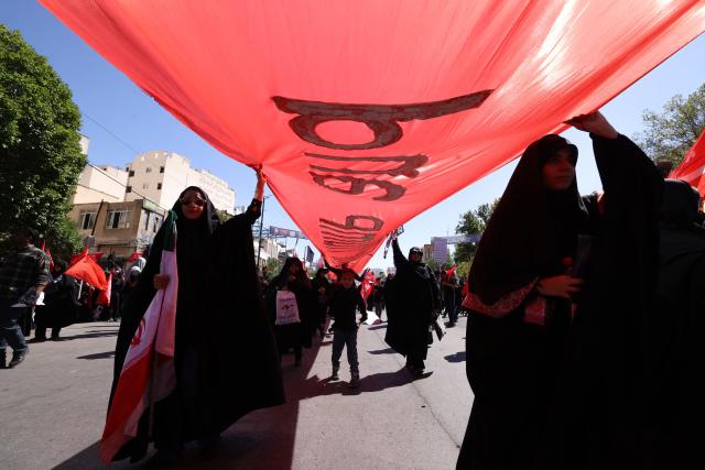 Mourners carry a banner during a funeral procession for Iran's slain supreme leader Ali Khamenei and members of his family, before he is buried at the Shrine of Imam Reza, Iran's most revered place of worship, in Mashhad on July 9, 2026. Braving sweltering heat and calling for revenge, Iranians loyal to the Islamic republic massed on July 9 for the burial of slain supreme leader Ali Khamenei in his hometown of Mashhad. (Photo by ATTA KENARE / AFP) / 