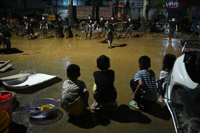 Children look on as security personnel clean mud from a road that was flooded when a reservoir collapsed in Gantang in China’s southwest Guangxi region on July 9, 2026. The death toll from devastating floods in southern China's Guangxi region rose to 39 on July 9, with nine people still missing, state media reported, as residents went about cleaning up. (Photo by GREG BAKER / AFP)