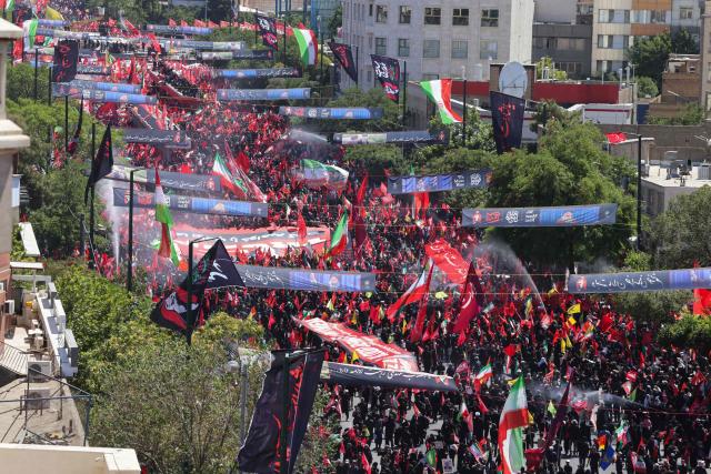Mourners march with flags and banners during a funeral procession for Iran's slain supreme leader Ali Khamenei and members of his family, before he is buried at the Shrine of Imam Reza, Iran's most revered place of worship, in Mashhad on July 9, 2026. Braving sweltering heat and calling for revenge, Iranians loyal to the Islamic republic massed on July 9 for the burial of slain supreme leader Ali Khamenei in his hometown of Mashhad. (Photo by ATTA KENARE / AFP) / 