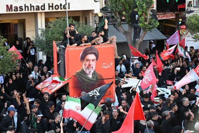 Crowds of mourners gather on a street around a portrait of Iran's supreme leader Mojtaba Khamenei ahead of the funeral procession of Iran's slain supreme leader Ali Khamenei and members of his family, before he is buried at the Shrine of Imam Reza, Iran's most revered place of worship, in Mashhad on July 9, 2026. Calling for revenge and rejecting any compromise with the West, Iranians loyal to the Islamic republic braved sweltering heat on July 9 to mass for the burial of supreme leader Ali Khamenei in his hometown of Mashhad. (Photo by Wakil Kohsar / AFP) / 