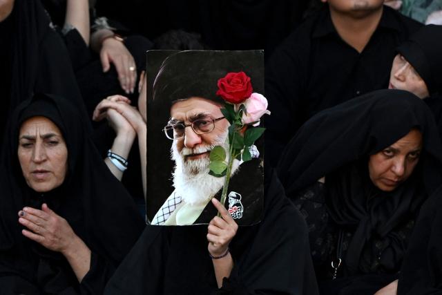 A woman holds flowers and a portrait of Iran's slain supreme leader Ali Khamenei as mourners gather ahead of his funeral procession and members of his family, before he is buried at the Shrine of Imam Reza, Iran's most revered place of worship, in Mashhad on July 9, 2026. Calling for revenge and rejecting any compromise with the West, Iranians loyal to the Islamic republic braved sweltering heat on July 9 to mass for the burial of supreme leader Ali Khamenei in his hometown of Mashhad. (Photo by Wakil Kohsar / AFP) / 
