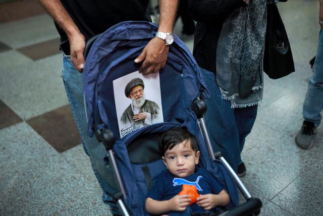 A man pushes a pram with a portrait of Iran's slain supreme leader Ali Khamenei as people arrive at a station ahead of his funeral procession and members of his family before his burial at the Shrine of Imam Reza, Iran's most revered place of worship, in Mashhad on July 9, 2026. Calling for revenge and rejecting any compromise with the West, Iranians loyal to the Islamic republic braved sweltering heat on July 9 to mass for the burial of supreme leader Ali Khamenei in his hometown of Mashhad. (Photo by AFP) / 