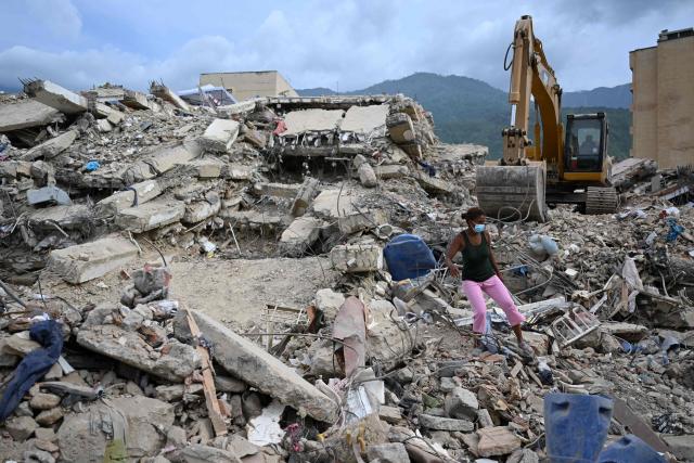 A woman walks over the rubble as a retroexcavator removes debris from collapsed buildings in Caraballeda, La Guaira state, Venezuela, on July 9, 2026 following the June 24 earthquakes. The United Nations launched an urgent appeal on July 8, 2026 for nearly $300 million towards Venezuela earthquake relief operations as the death toll from the disaster rose to more than 3,800 people. (Photo by Raul ARBOLEDA / AFP)