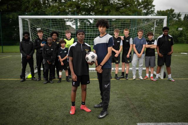 Fabian Myers (centre right) and Kaziah Cameron (centre left), year 9 students at Our Lady & St Chad Catholic School, who participate in the 'Football Beyond Borders' programme, pose for a photograph after playing a football match with fellow FBB students in Wolverhampton, central England on June 12, 2026. FBB (Football Beyond Borders) works with young people from areas of socio-economic disadvantage who are disengaged at school but passionate about football, to help them finish school with the skills and grades to make a successful transition into adulthood. (Photo by Oli SCARFF / AFP) / TO GO WITH AFP STORY BY Alexandra Del PERAL