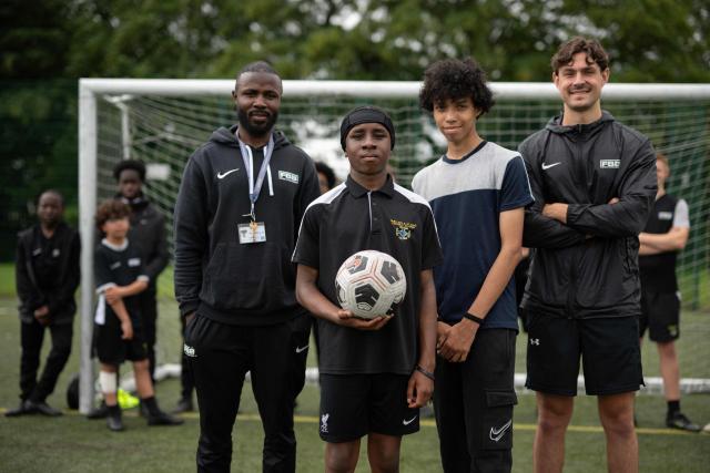 Matt Bishop (R) and Ezektel Agyemang (L), members of staff with 'Football Beyond Borders', pose with year 9 students Fabian Myers (2nd R) and Kaziah Cameron (2nd L), after coaching a football match with FBB students at Our Lady & St Chad Catholic School, in Wolverhampton, central England on June 12, 2026. FBB (Football Beyond Borders) works with young people from areas of socio-economic disadvantage who are disengaged at school but passionate about football, to help them finish school with the skills and grades to make a successful transition into adulthood. (Photo by Oli SCARFF / AFP) / TO GO WITH AFP STORY BY Alexandra Del PERAL