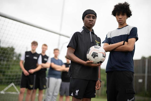 Fabian Myers (R) and Kaziah Cameron (2nd R), year 9 students at Our Lady & St Chad Catholic School, who participate in the 'Football Beyond Borders' programme, pose for a photograph after playing a football match with fellow FBB students in Wolverhampton, central England on June 12, 2026. FBB (Football Beyond Borders) works with young people from areas of socio-economic disadvantage who are disengaged at school but passionate about football, to help them finish school with the skills and grades to make a successful transition into adulthood. (Photo by Oli SCARFF / AFP) / TO GO WITH AFP STORY BY Alexandra Del PERAL