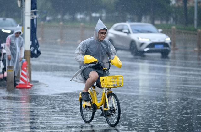A man wearing a raincoat rides a sharing bicycle along a street on a rainy day in Beijing on July 10, 2026. (Photo by WANG Zhao / AFP)