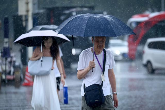 People holding umbrella cross a street on a rainy day in Beijing on July 10, 2026. (Photo by WANG Zhao / AFP)