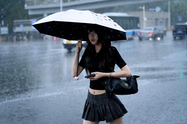 A woman holding an umbrella walks along a road on a rainy day in Beijing on July 10, 2026. (Photo by WANG Zhao / AFP)