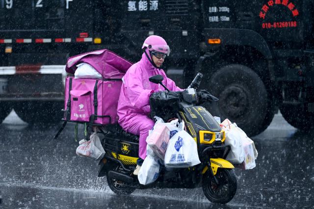 A delivery man rides his electric motorcycle along a road on a rainy day in Beijing on July 10, 2026. (Photo by WANG Zhao / AFP)