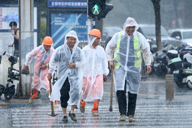 A group of workers wearing raincoat cross a street on a rainy day in Beijing on July 10, 2026. (Photo by WANG Zhao / AFP)
