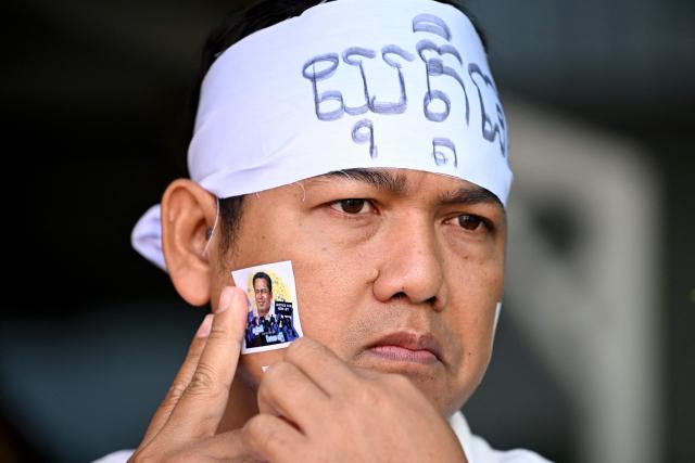 A man places a sticker of an image of former prominent Cambodian critic Kem ley during the 10th anniversary of his murder at a gasoline station in Phnom Penh on July 10, 2026. (Photo by TANG CHHIN Sothy / AFP)