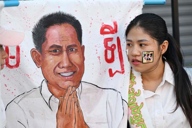 A woman holds an image of former prominent Cambodian critic Kem ley as she speaks to her friend during the 10th anniversary of his murder at a gasoline station in Phnom Penh on July 10, 2026. (Photo by TANG CHHIN Sothy / AFP)