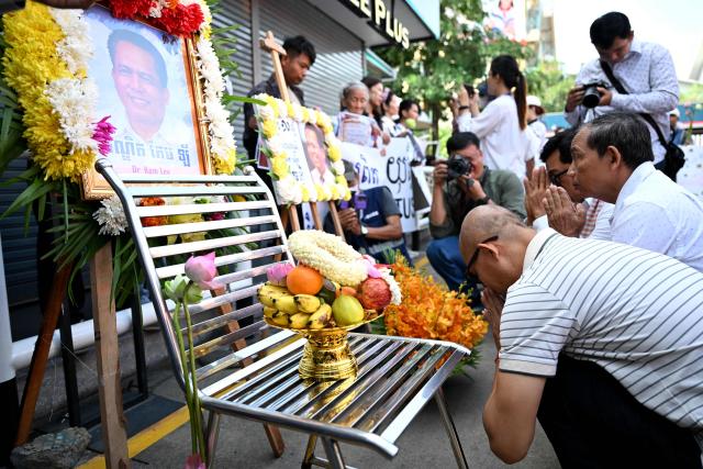People pray in front of images of former prominent Cambodian critic Kem ley during the 10th anniversary of his murder at a gasoline station in Phnom Penh on July 10, 2026. (Photo by TANG CHHIN Sothy / AFP)