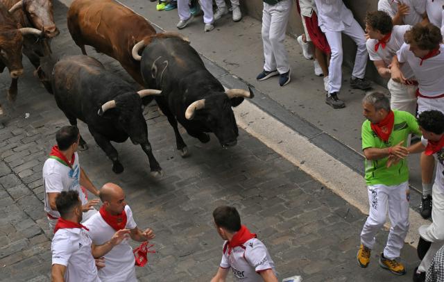 Participants run ahead of bulls during the fourth running of the bulls of the San Fermin festival in Pamplona, northern Spain, on July 10, 2026. Thousands of people every year attend the week-long festival and its famous 'encierros', or running of the bulls, in which six bulls are released at 8:00 a.m. evey day to run from their corral to the bullring through the narrow streets of the old town over an 850 meters (yards) course while runners ahead of them try to stay close to the bulls without falling over or being gored. (Photo by JORGE GUERRERO / AFP)