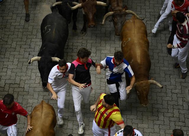 Participants run ahead of bulls during the fourth running of the bulls of the San Fermin festival in Pamplona, northern Spain, on July 10, 2026. Thousands of people every year attend the week-long festival and its famous 'encierros', or running of the bulls, in which six bulls are released at 8:00 a.m. evey day to run from their corral to the bullring through the narrow streets of the old town over an 850 meters (yards) course while runners ahead of them try to stay close to the bulls without falling over or being gored. (Photo by ANDER GILLENEA / AFP)