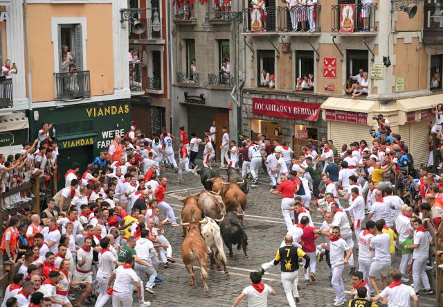 Participants run ahead of bulls during the fourth running of the bulls of the San Fermin festival in Pamplona, northern Spain, on July 10, 2026. Thousands of people every year attend the week-long festival and its famous 'encierros', or running of the bulls, in which six bulls are released at 8:00 a.m. evey day to run from their corral to the bullring through the narrow streets of the old town over an 850 meters (yards) course while runners ahead of them try to stay close to the bulls without falling over or being gored. (Photo by JORGE GUERRERO / AFP)