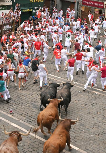 Participants run ahead of bulls during the fourth running of the bulls of the San Fermin festival in Pamplona, northern Spain, on July 10, 2026. Thousands of people every year attend the week-long festival and its famous 'encierros', or running of the bulls, in which six bulls are released at 8:00 a.m. evey day to run from their corral to the bullring through the narrow streets of the old town over an 850 meters (yards) course while runners ahead of them try to stay close to the bulls without falling over or being gored. (Photo by JORGE GUERRERO / AFP)