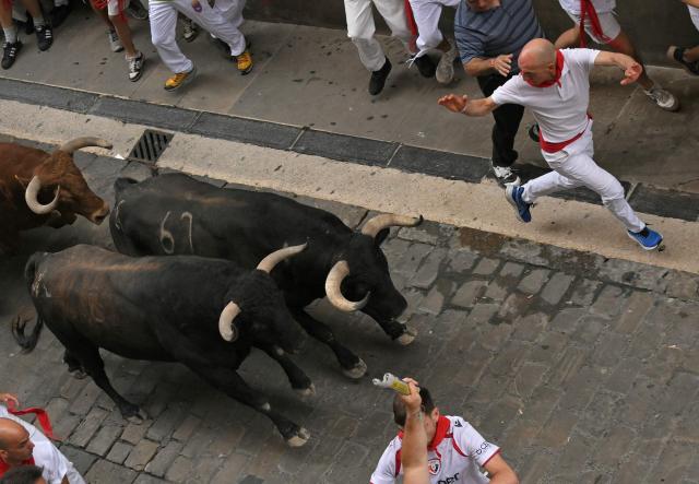 Participants run ahead of bulls during the fourth running of the bulls of the San Fermin festival in Pamplona, northern Spain, on July 10, 2026. Thousands of people every year attend the week-long festival and its famous 'encierros', or running of the bulls, in which six bulls are released at 8:00 a.m. evey day to run from their corral to the bullring through the narrow streets of the old town over an 850 meters (yards) course while runners ahead of them try to stay close to the bulls without falling over or being gored. (Photo by JORGE GUERRERO / AFP)