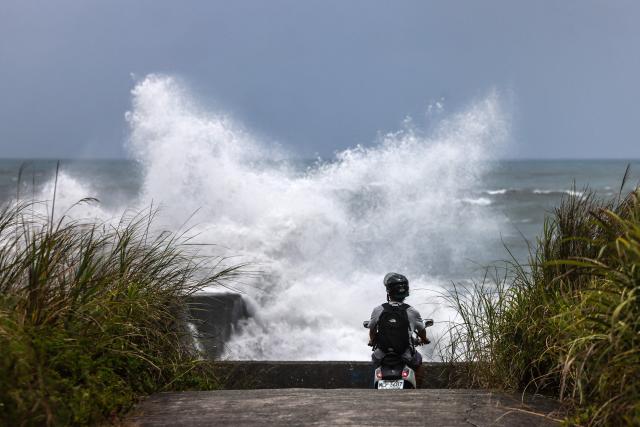 A man rides his motorbike as strong waves break along the coast in Yilan on July 10, 2026, as Typhoon Bavi moves toward Northeastern Taiwan. (Photo by I-Hwa Cheng / AFP)