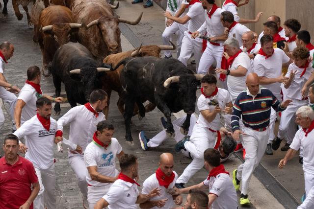 Participants run ahead of bulls during the fourth running of the bulls of the San Fermin festival in Pamplona, northern Spain, on July 10, 2026. Thousands of people every year attend the week-long festival and its famous 'encierros', or running of the bulls, in which six bulls are released at 8:00 a.m. evey day to run from their corral to the bullring through the narrow streets of the old town over an 850 meters (yards) course while runners ahead of them try to stay close to the bulls without falling over or being gored. (Photo by JORGE GUERRERO / AFP)