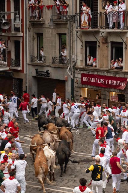 Participants run ahead of bulls during the fourth running of the bulls of the San Fermin festival in Pamplona, northern Spain, on July 10, 2026. Thousands of people every year attend the week-long festival and its famous 'encierros', or running of the bulls, in which six bulls are released at 8:00 a.m. evey day to run from their corral to the bullring through the narrow streets of the old town over an 850 meters (yards) course while runners ahead of them try to stay close to the bulls without falling over or being gored. (Photo by JORGE GUERRERO / AFP)