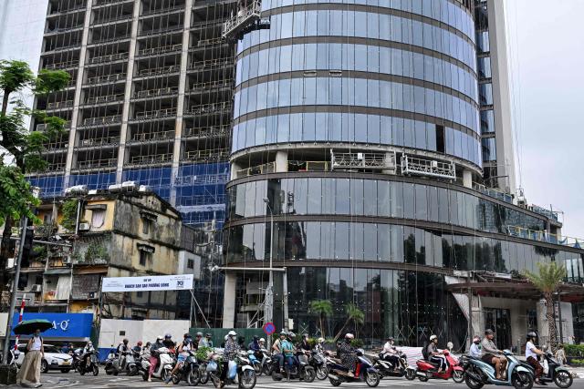 People ride their motorbike past a hotel construction site in Hanoi on July 10, 2026. (Photo by Nhac NGUYEN / AFP)
