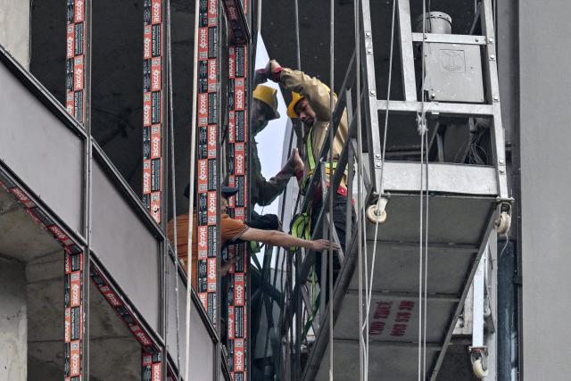Workers install a pane of glass at a hotel construction site in Hanoi on July 10, 2026. (Photo by Nhac NGUYEN / AFP)